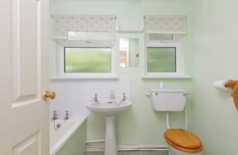 Bright mint green bathroom with white pedestal sink, wooden toilet seat, small window above sink, and minimalist fixtures on white wall