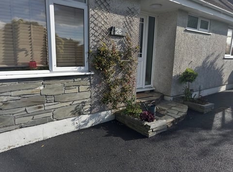 Modern house exterior with stone cladding, white-framed windows, doors, and a small paved patio area with potted plants
