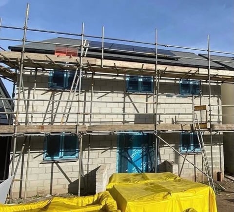 Construction site with two-story building covered by metal scaffolding and yellow safety netting under clear blue sky