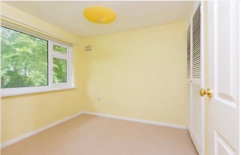Empty bedroom with pale yellow walls, beige carpet, window with green view, yellow ceiling light, and open closet door
