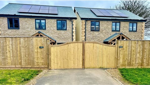 Modern stone townhouses with solar panels on roof and wooden gate entrance to driveway