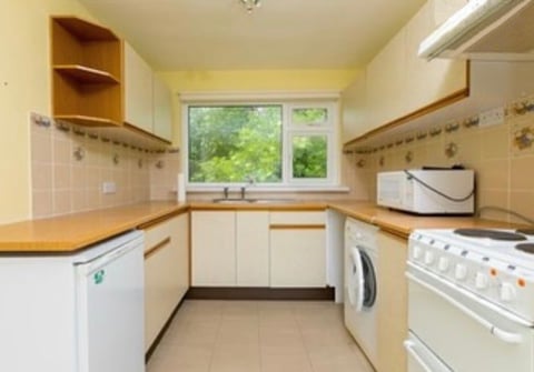 Small galley kitchen with cream cabinets, wooden worktops, white appliances, and window overlooking garden
