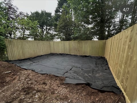 Black ground cover fabric laid out in a fenced yard surrounded by trees and mulch