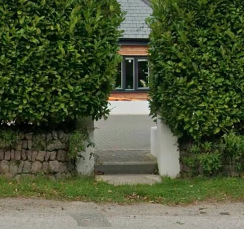 House entrance framed by lush green hedges with brick and white walls, set back from a driveway