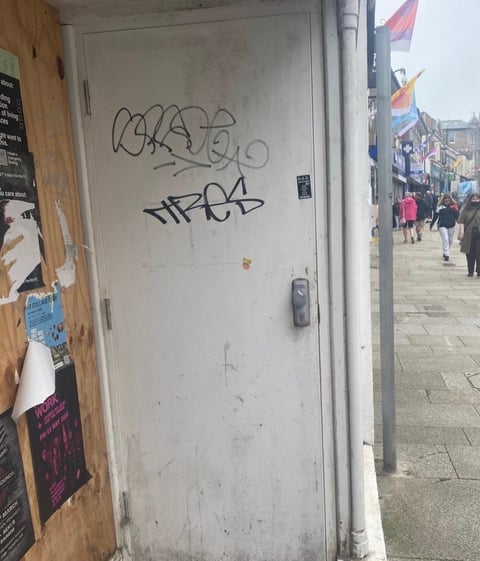 White door with graffiti and stickers on urban street with pedestrians and flags in background
