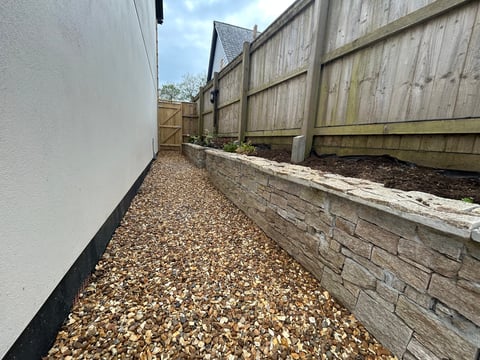 Narrow gravel pathway between white house wall and weathered wooden fence in residential yard