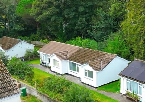 Aerial view of a modern white bungalow with brown tiled roof surrounded by green lawn and dense trees