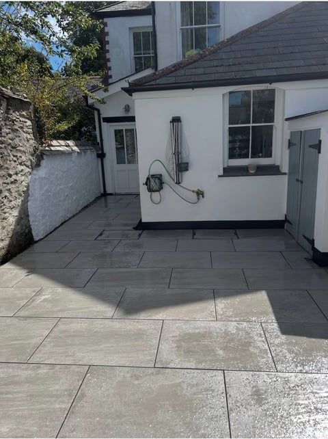 Contemporary patio with gray stone paving beside white cottage with dark roof and garden walls