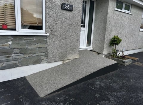 Modern house entrance with gray stone driveway, white-framed door numbered 26, and small potted plant beside the entrance