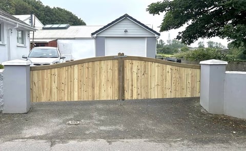Wooden driveway gate with white pillars leading to residential home with garage and trees