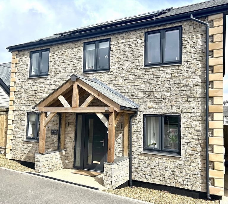Modern stone house with wooden porch entrance, black-framed windows, and slate roof